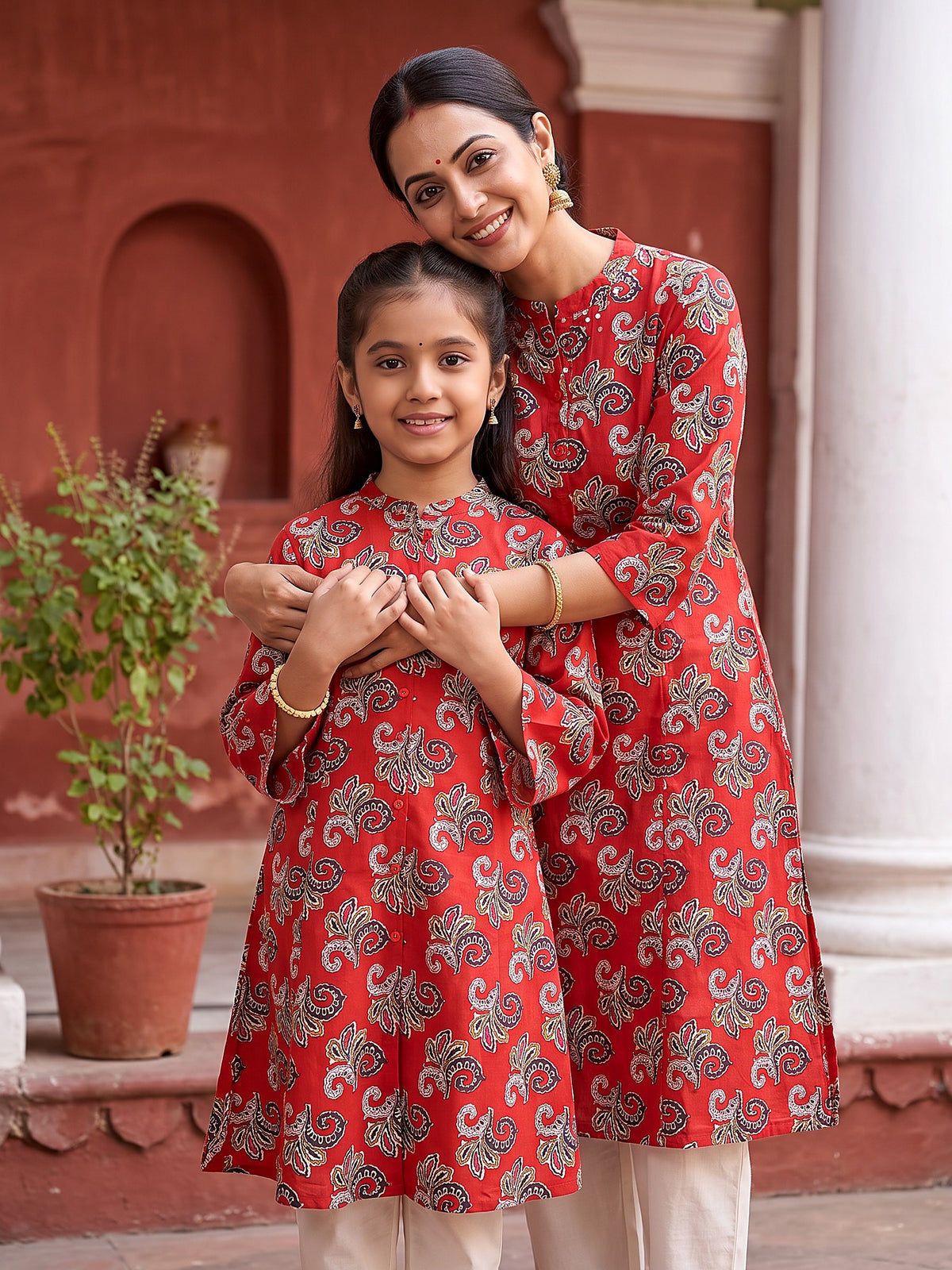 Mother hugging daughter in matching bold red kurtis